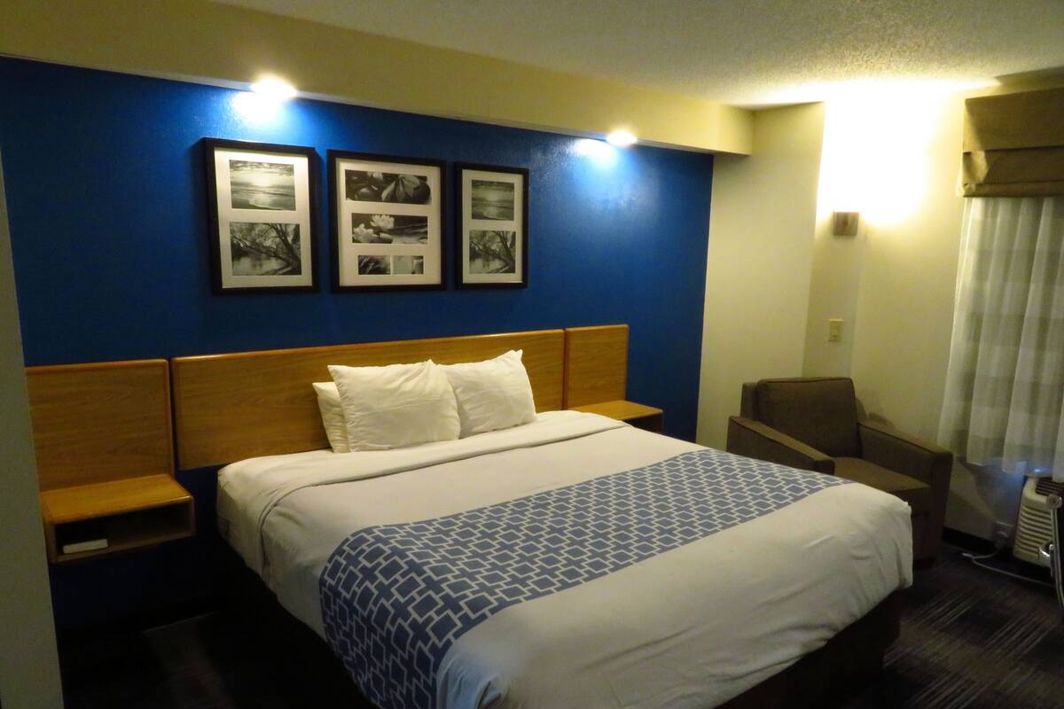 A hotel room with a large bed, wooden headboard, white bedding, and three framed photographs on the wall.