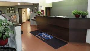 A reception area with a reception desk, a clock, and a doormat indicating the location. - Rodeway Inn Austell Six Flags (Austell)