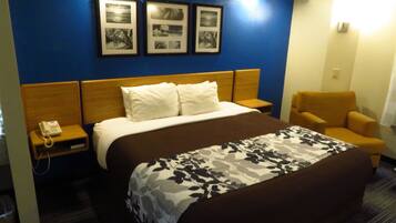 Une chambre d’hôtel avec un lit, une chaise, une table de chevet avec un téléphone et des tableaux encadrés au mur.
