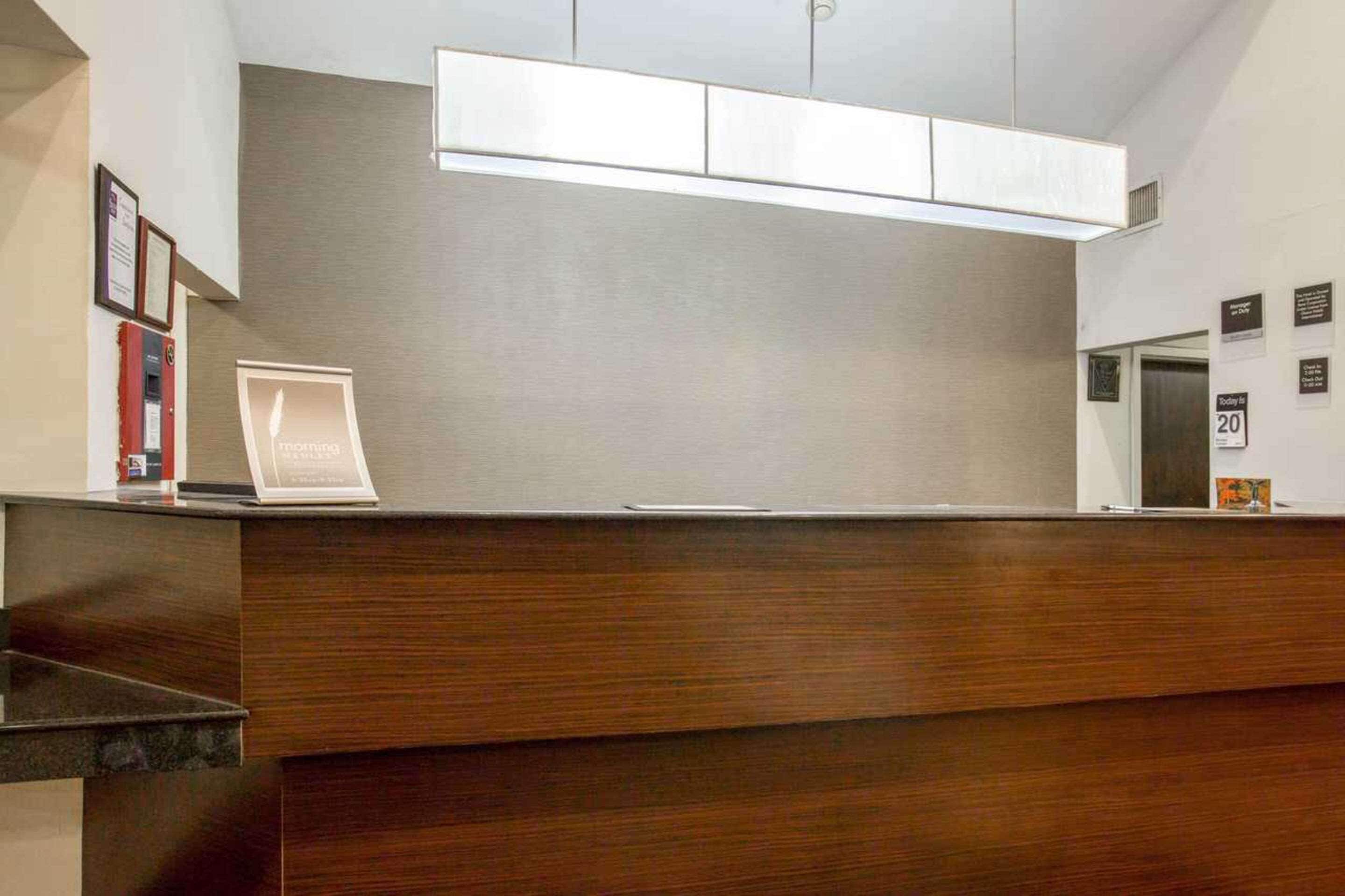 Un mostrador de recepción con una computadora portátil, certificados enmarcados y un cartel que indica la disponibilidad de habitaciones.