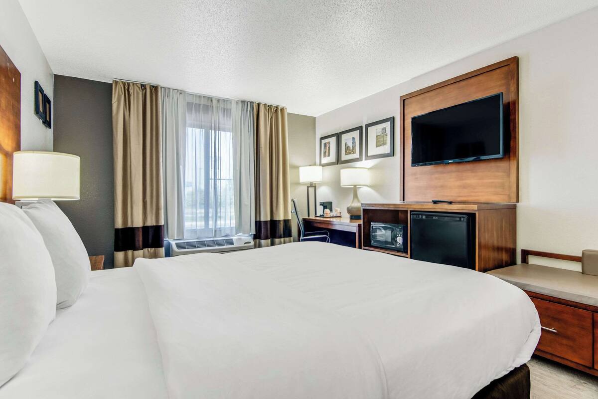 A hotel room with a large bed, a desk with a computer, a television, and a window with curtains.