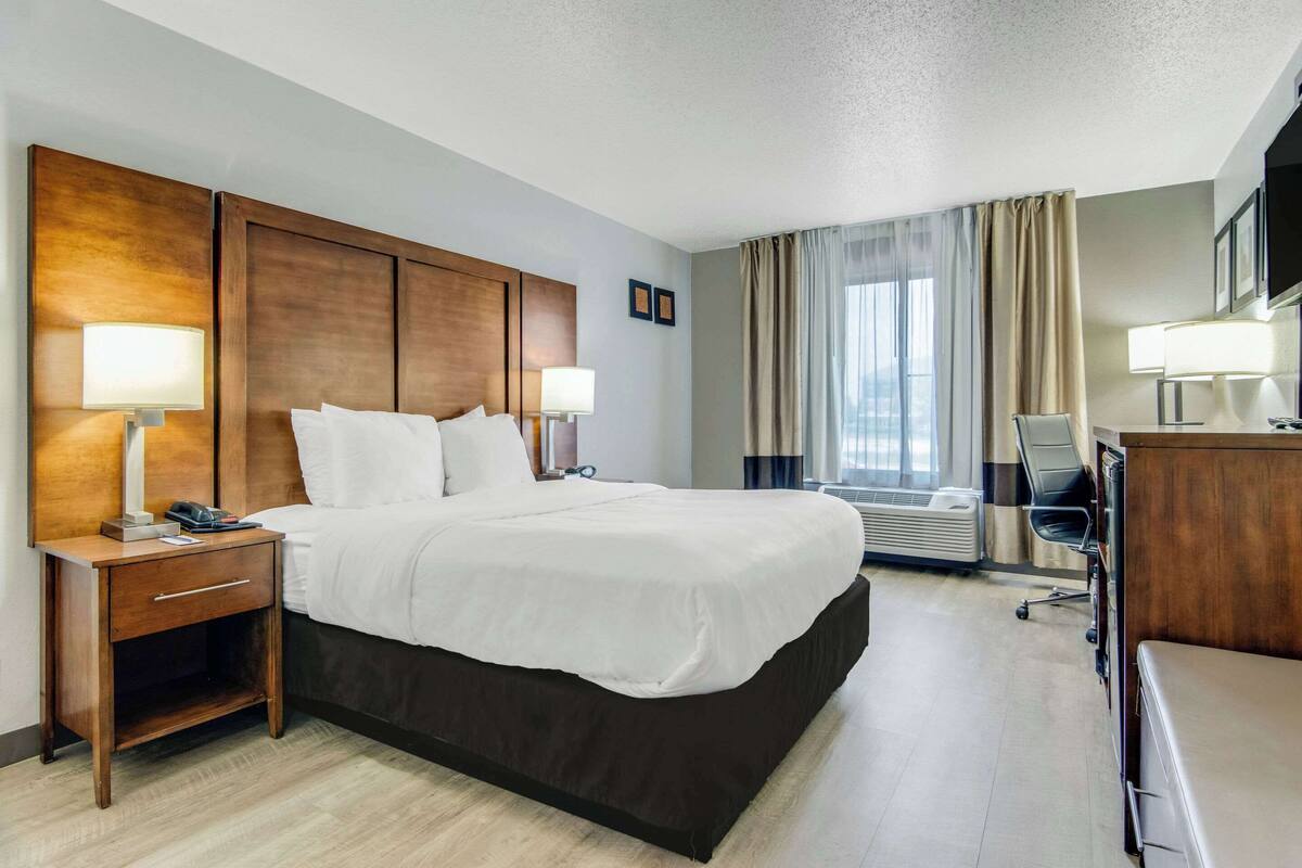 A hotel room with a large bed, two bedside lamps, a desk with a chair, and a TV.