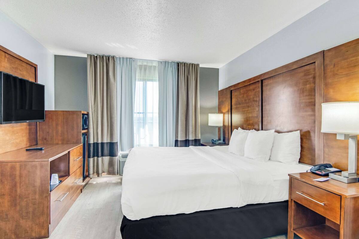 A hotel room with a large bed, wooden headboard, bedside tables with lamps, a TV, and a desk with drawers.