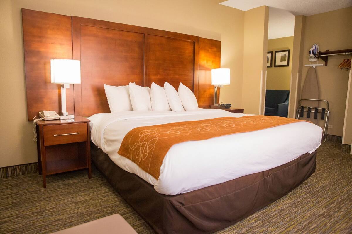 A hotel room with a large bed, two bedside lamps, a desk with a telephone, and a chair.