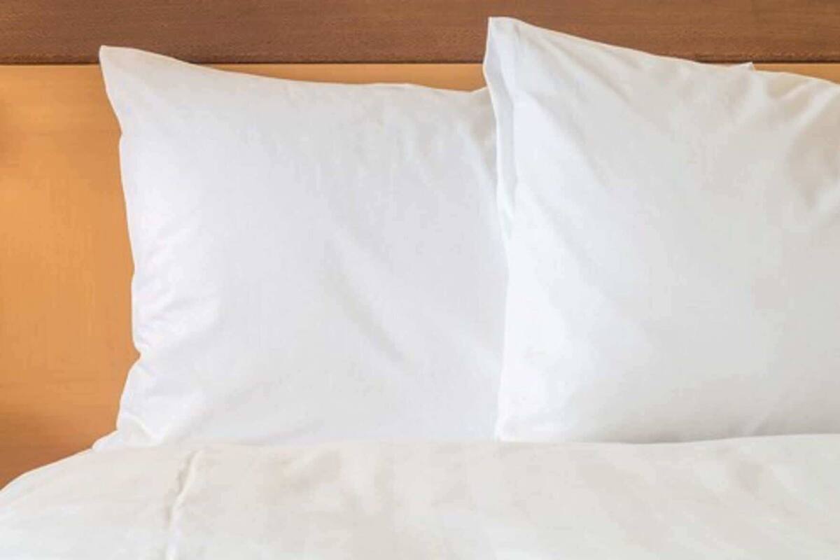 A bed with white bedding and pillows against a wooden headboard.
