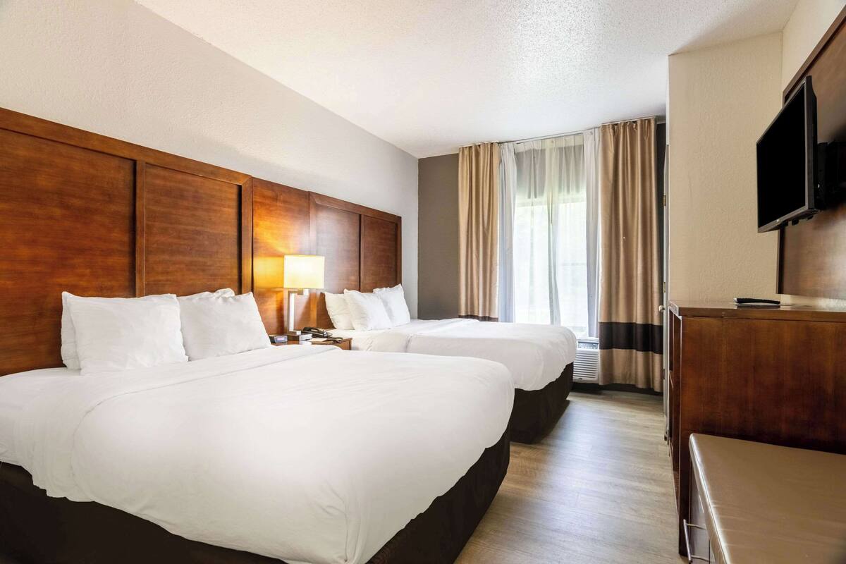 A hotel room with two beds, a wooden headboard, a flat-screen TV, and a window with curtains.