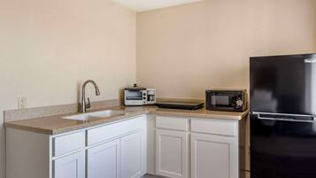 A compact kitchen with white cabinets, a stainless steel sink, a toaster, a microwave, and a black refrigerator.