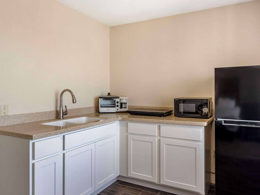 A compact kitchen with white cabinets, a stainless steel sink, a toaster, a microwave, and a black refrigerator.