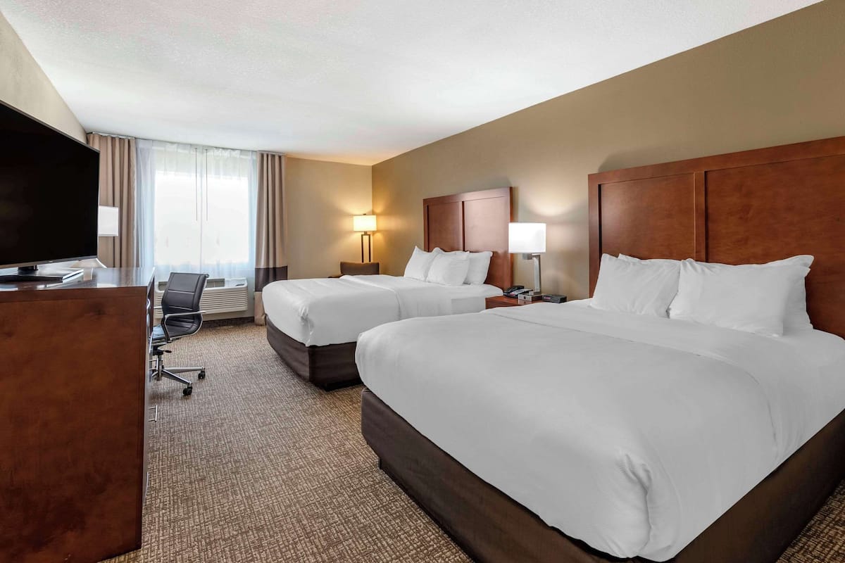 A hotel room with two beds, a desk, a TV, and a chair.