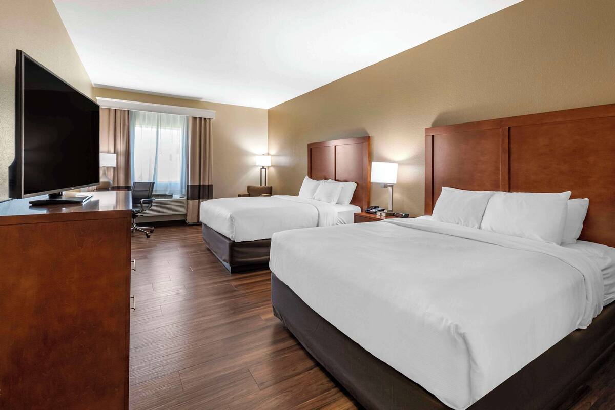 A hotel room with two beds, a desk with a flat-screen TV, a laptop, and a chair.