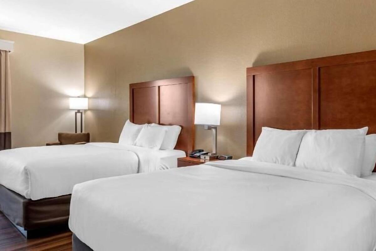 A hotel room with two beds, a nightstand with a lamp, and a window with curtains.