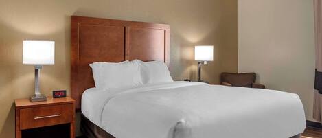 Habitación de hotel con una cama grande, cabecero de madera, dos mesitas de noche con lámparas y una pequeña silla.