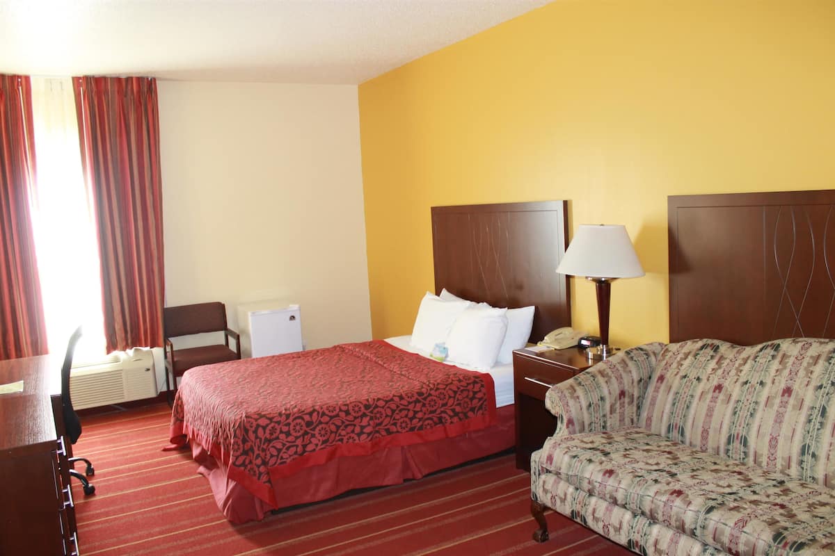 A hotel room with a bed, a sofa, a desk, and a lamp.