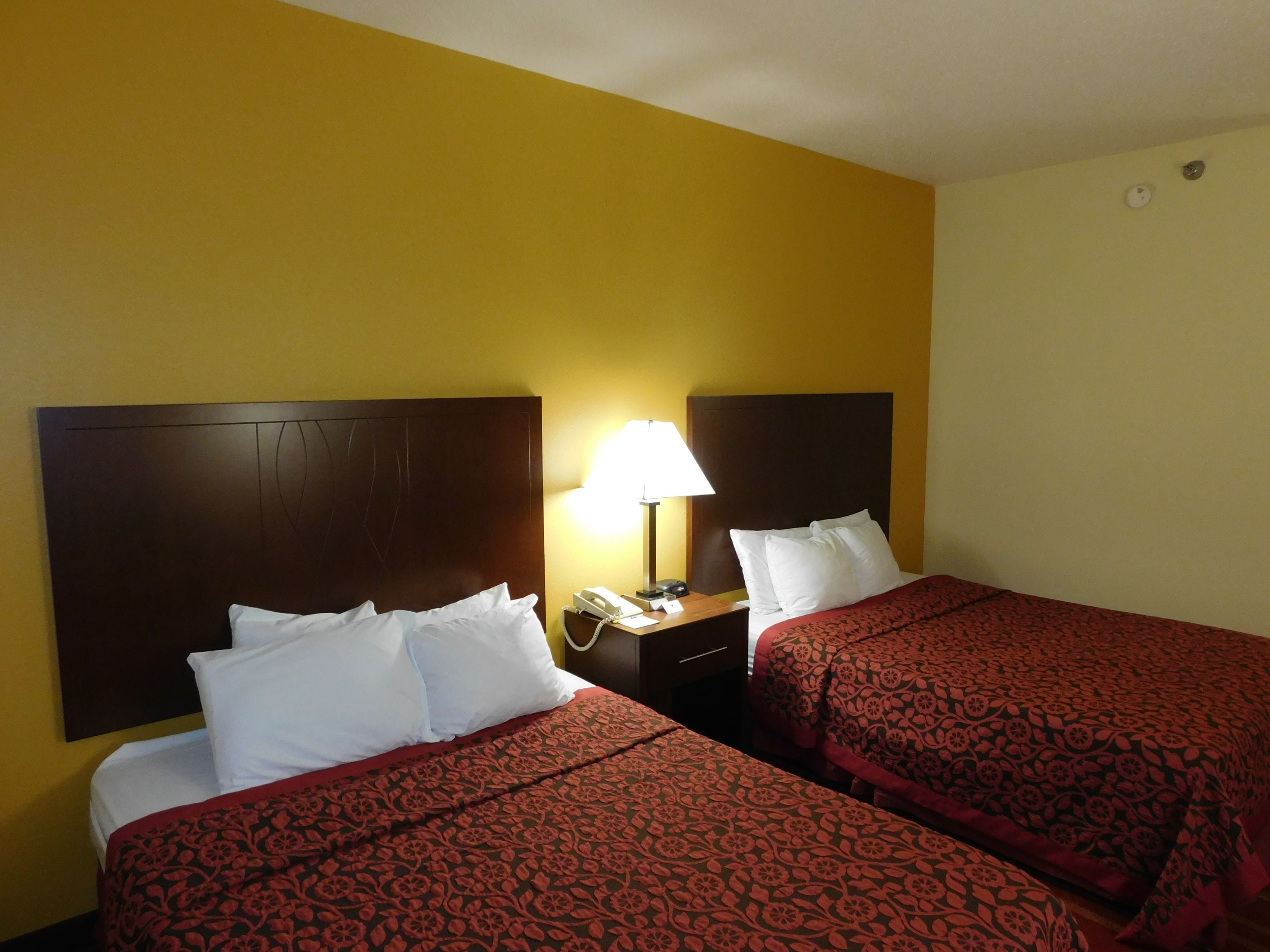 Ein Hotelzimmer mit zwei Betten, jeweils mit einem Holzkopfteil, einem Nachttisch mit Lampe und Telefon.