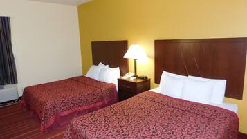 A hotel room with two beds, each with a red patterned bedspread and white pillows. There is a wooden headboard on each bed, and a nightstand with a lamp and a telephone.