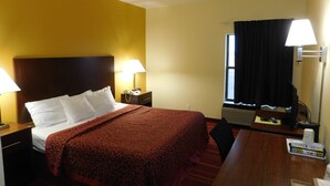 A hotel room with a bed, bedside tables, a desk, a chair, a window with curtains, and a lamp. - Days Inn by Wyndham Walcott Davenport (Walcott)