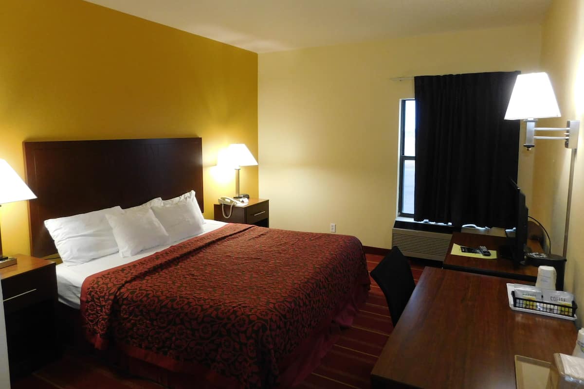 A hotel room with a bed, bedside tables, a desk, a chair, a window with curtains, and a lamp.