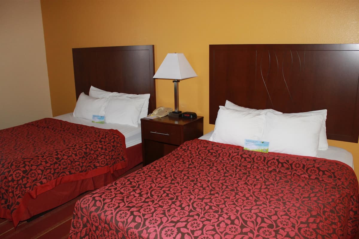 Two single beds with red floral bedspreads, a nightstand with a lamp, and a wall clock.