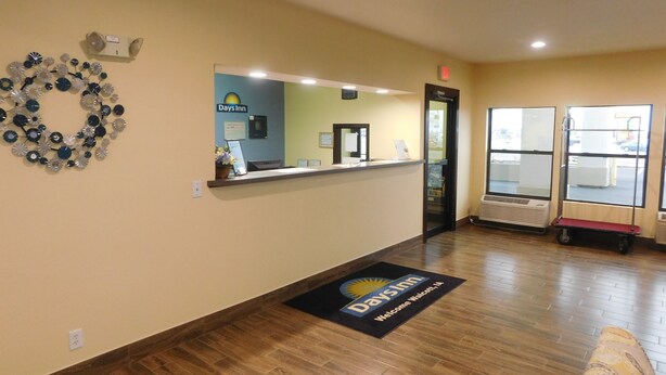 A reception area with a desk, a mirror, a Days Inn sign, a decorative wall piece, and a welcome mat. - Days Inn by Wyndham Walcott Davenport (Walcott)
