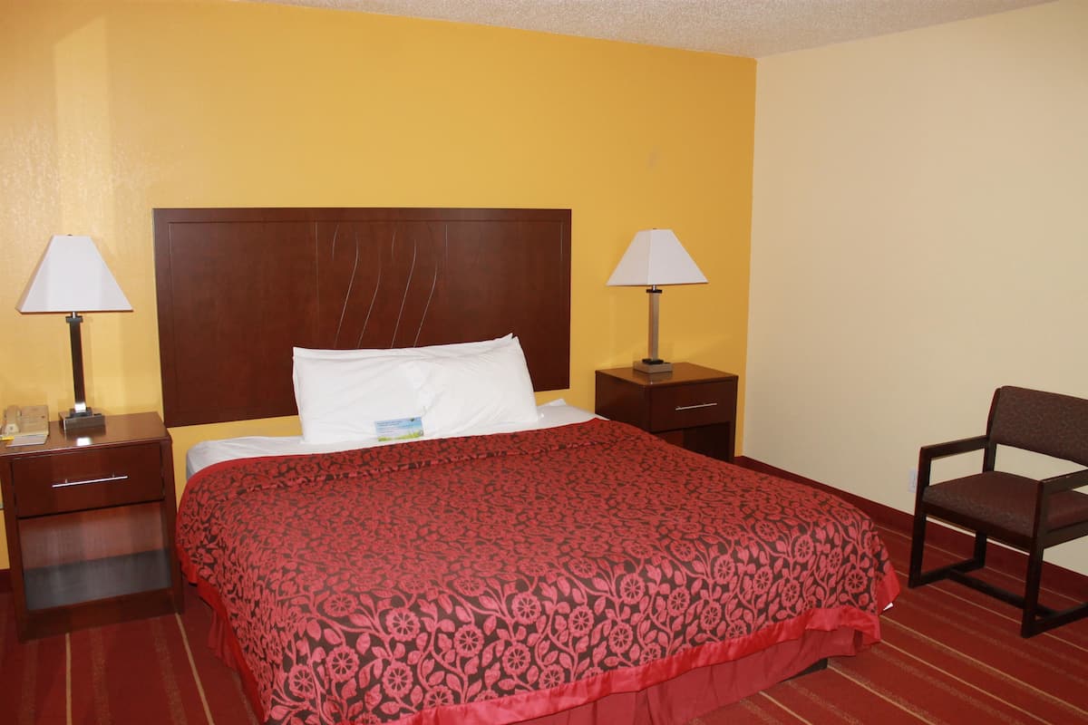 A hotel room with a large bed, two bedside tables with lamps, a chair, and a wooden headboard.