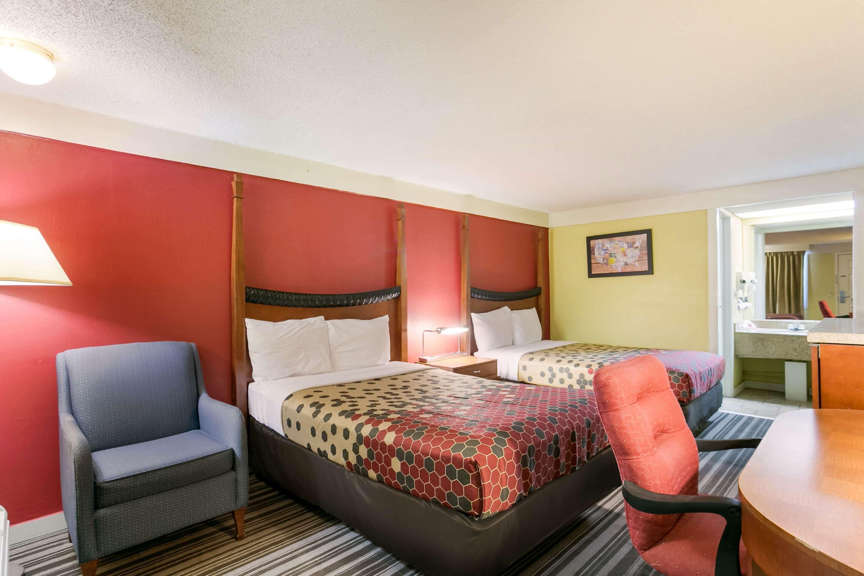 A hotel room with two beds, a chair, a desk, and a mirror.
