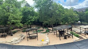 Un parc équipé de tables de pique-nique, d’un petit terrain de basket et d’une aire de jeux entourée d’arbres.