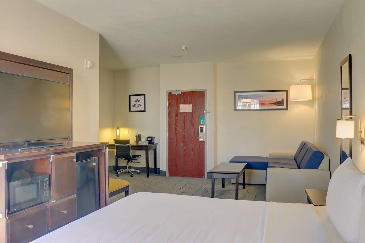 Quarto de hotel com cama, escrivaninha, cadeira, televisão e micro-ondas.