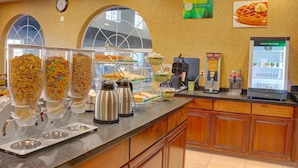 A breakfast bar with cereal dispensers, waffle maker, and a refrigerator. - Quality Inn & Suites Roswell North (Roswell)