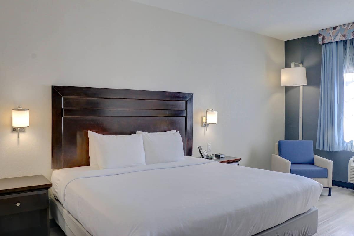 Quarto de hotel com uma cama grande, mesas de cabeceira, uma cadeira e um abajur.