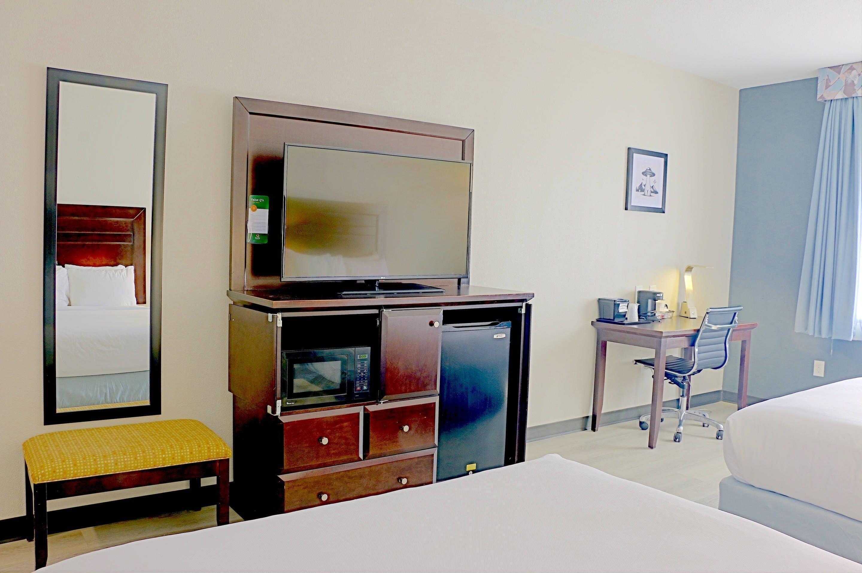 Ein Hotelzimmer mit einem Bett, einem Schreibtisch mit Stuhl, einem Fernseher, einer Mikrowelle und einem Kühlschrank.