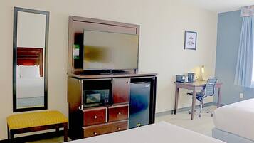 Ein Hotelzimmer mit einem Bett, einem Schreibtisch mit Stuhl, einem Fernseher, einer Mikrowelle und einem Kühlschrank.