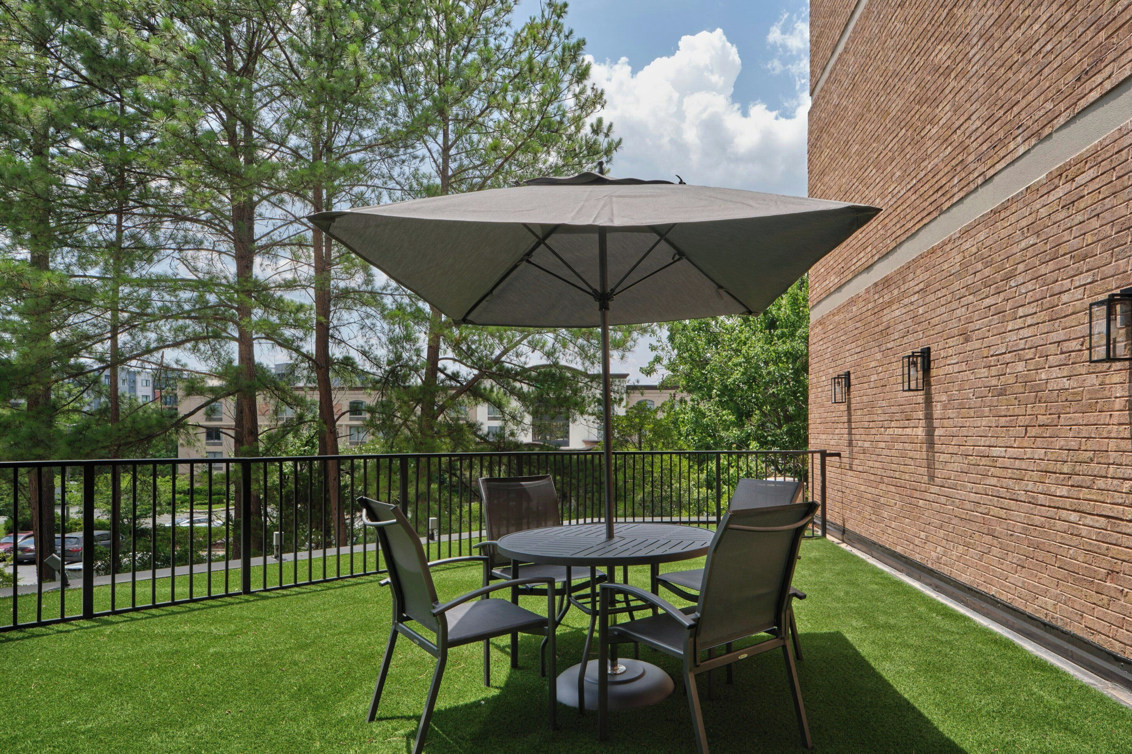 A patio with a round table and chairs, a large umbrella, and a brick wall.