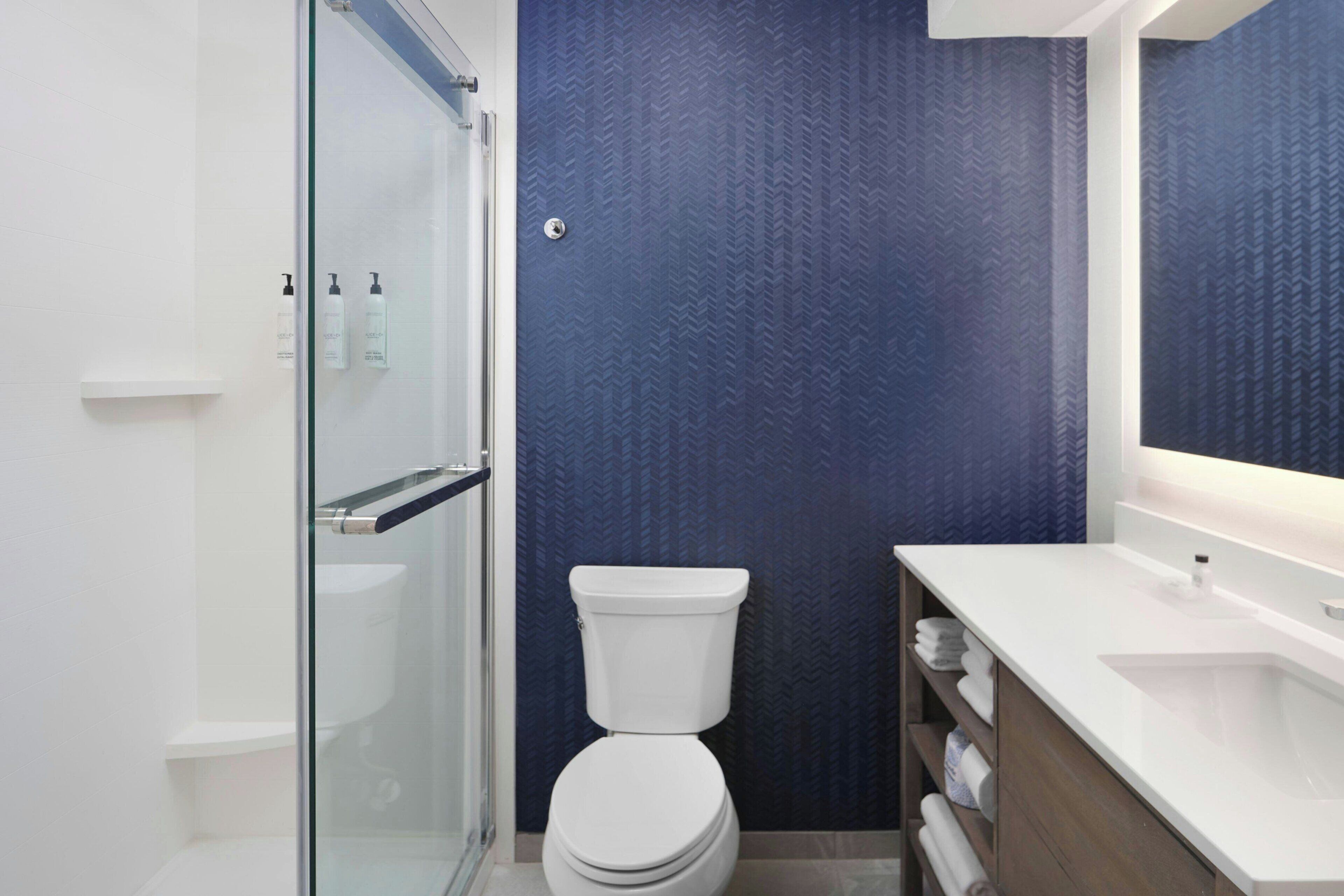 A modern bathroom with a glass shower enclosure, a white toilet, and a wooden vanity with a sink.