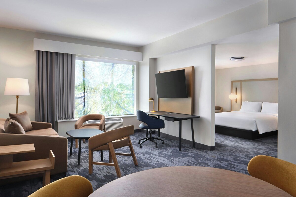 A hotel room with a bed, a desk, a chair, a sofa, and a TV.