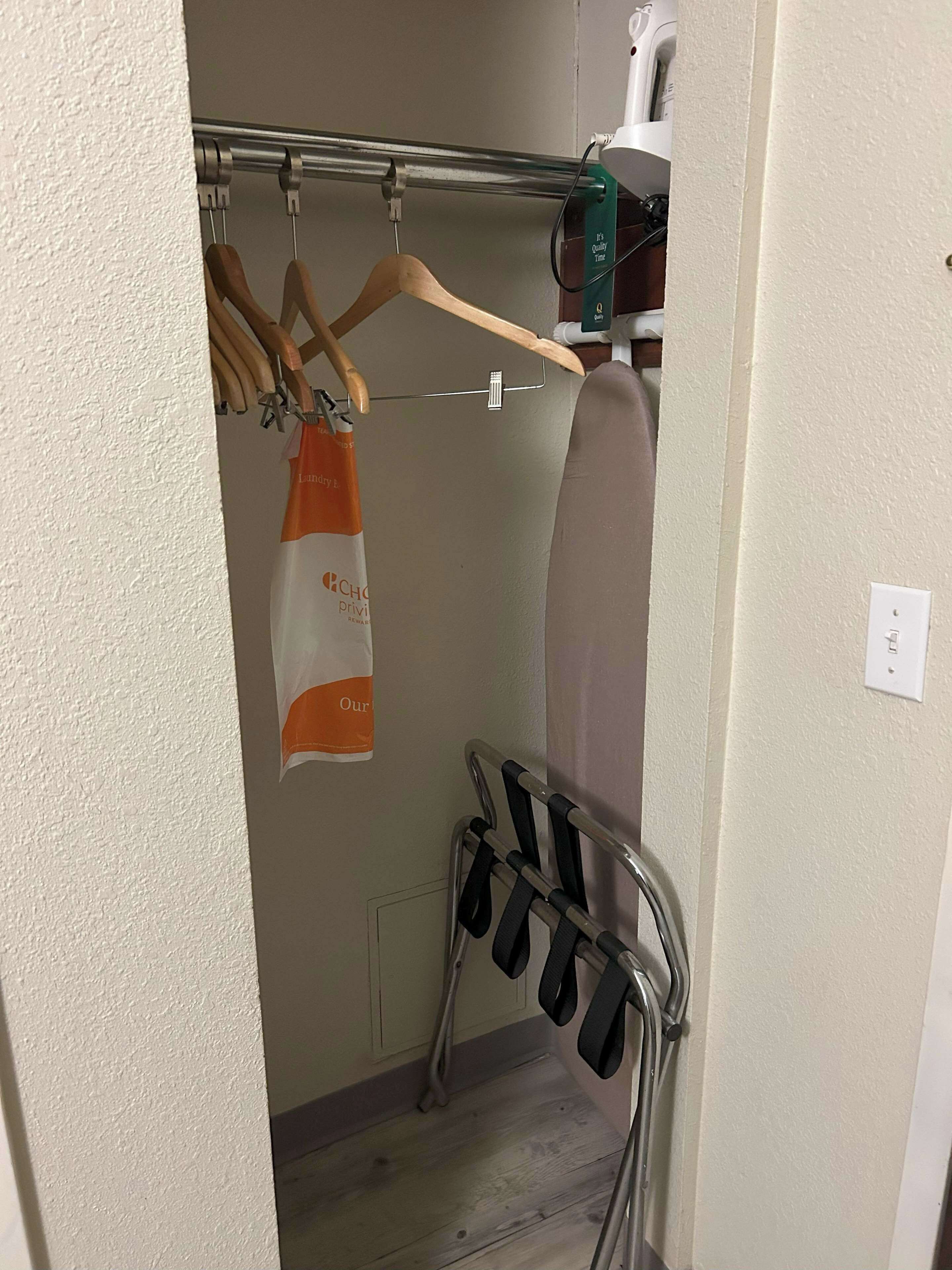 A small laundry area with a drying rack, an ironing board, and a hanging clothes rack.