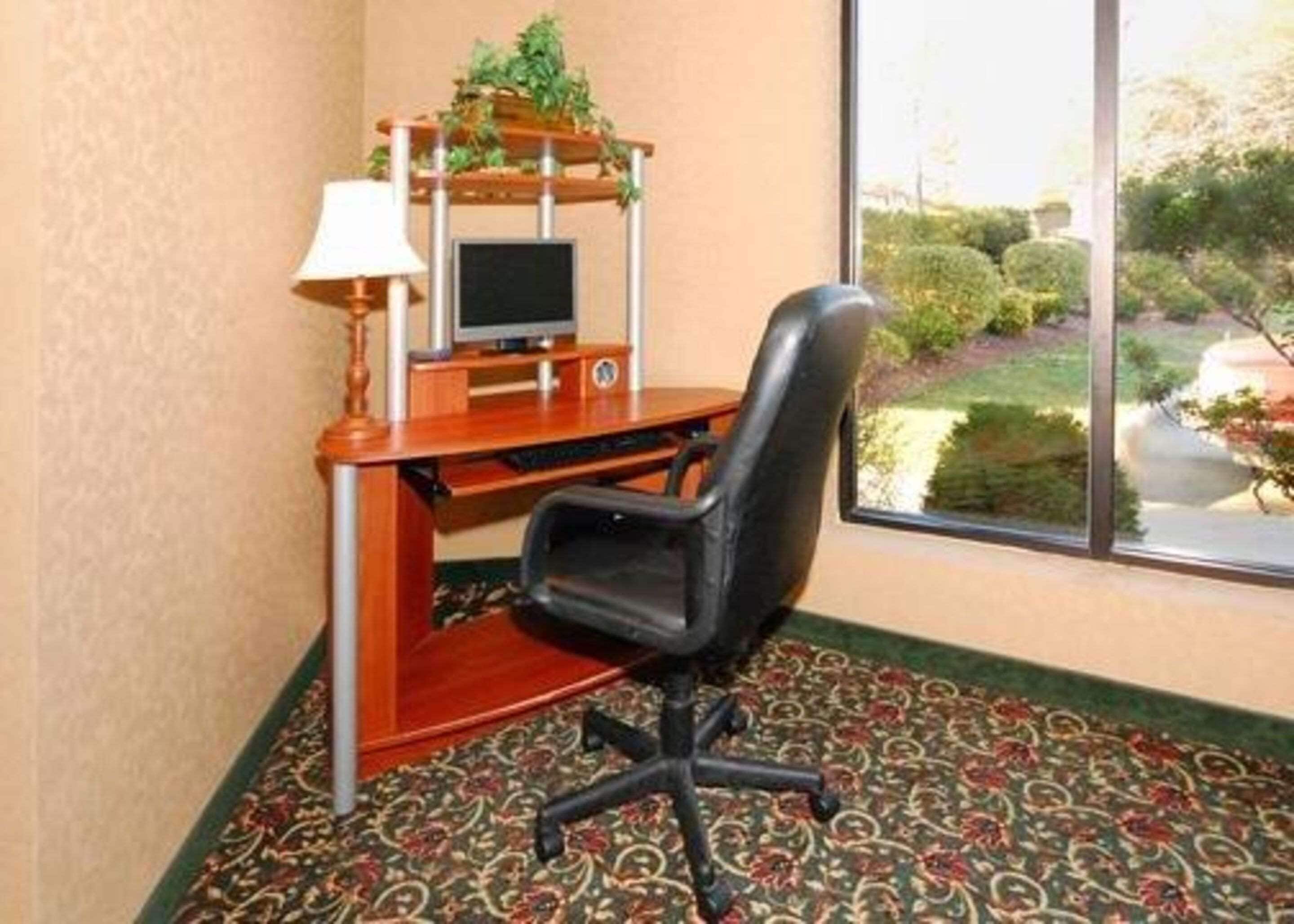 Ein kleines Büro mit Schreibtisch, Stuhl, Computer und einem Fenster mit Gartenblick.