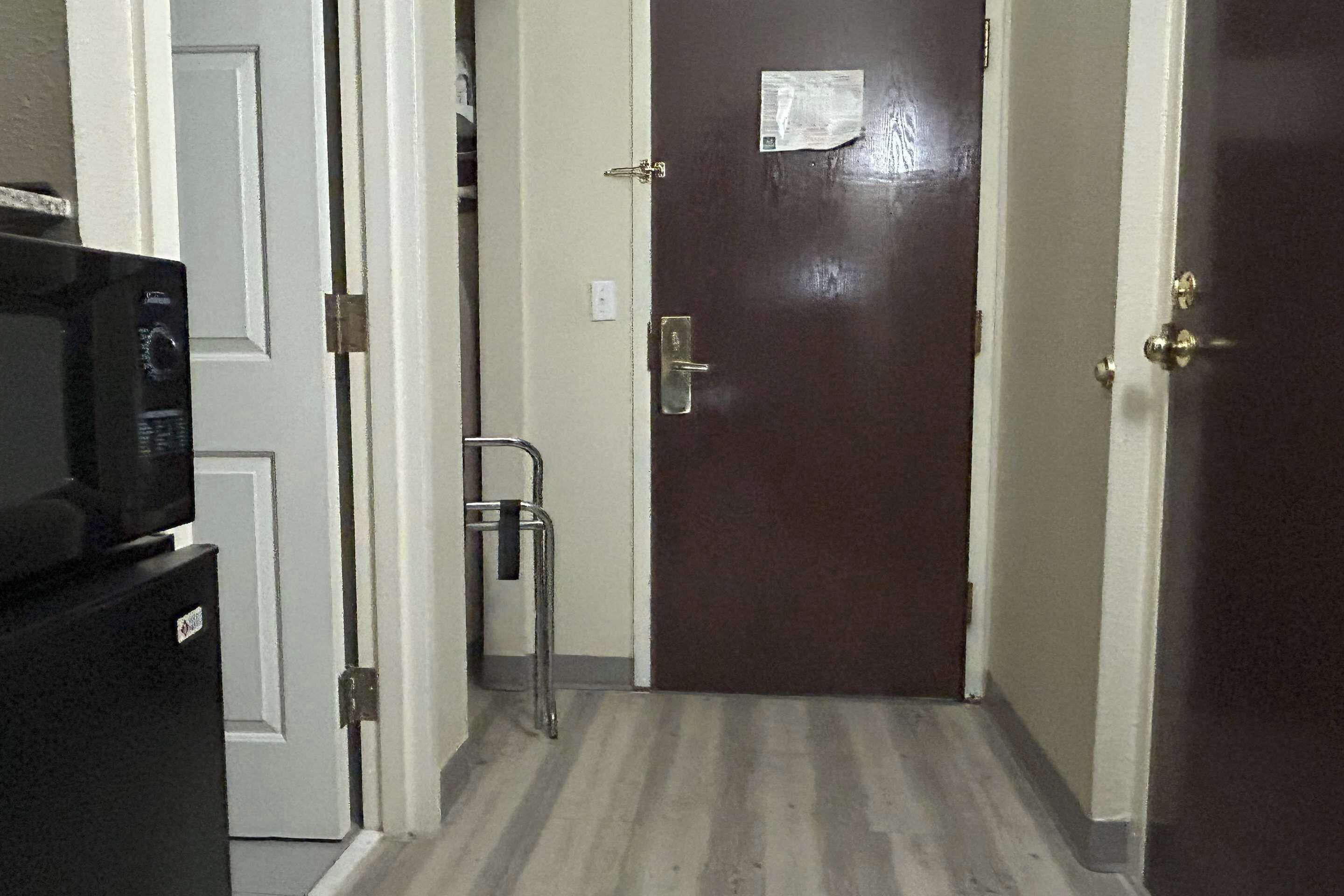 A narrow hallway with a dark brown door, a white door, and a black refrigerator on the left.