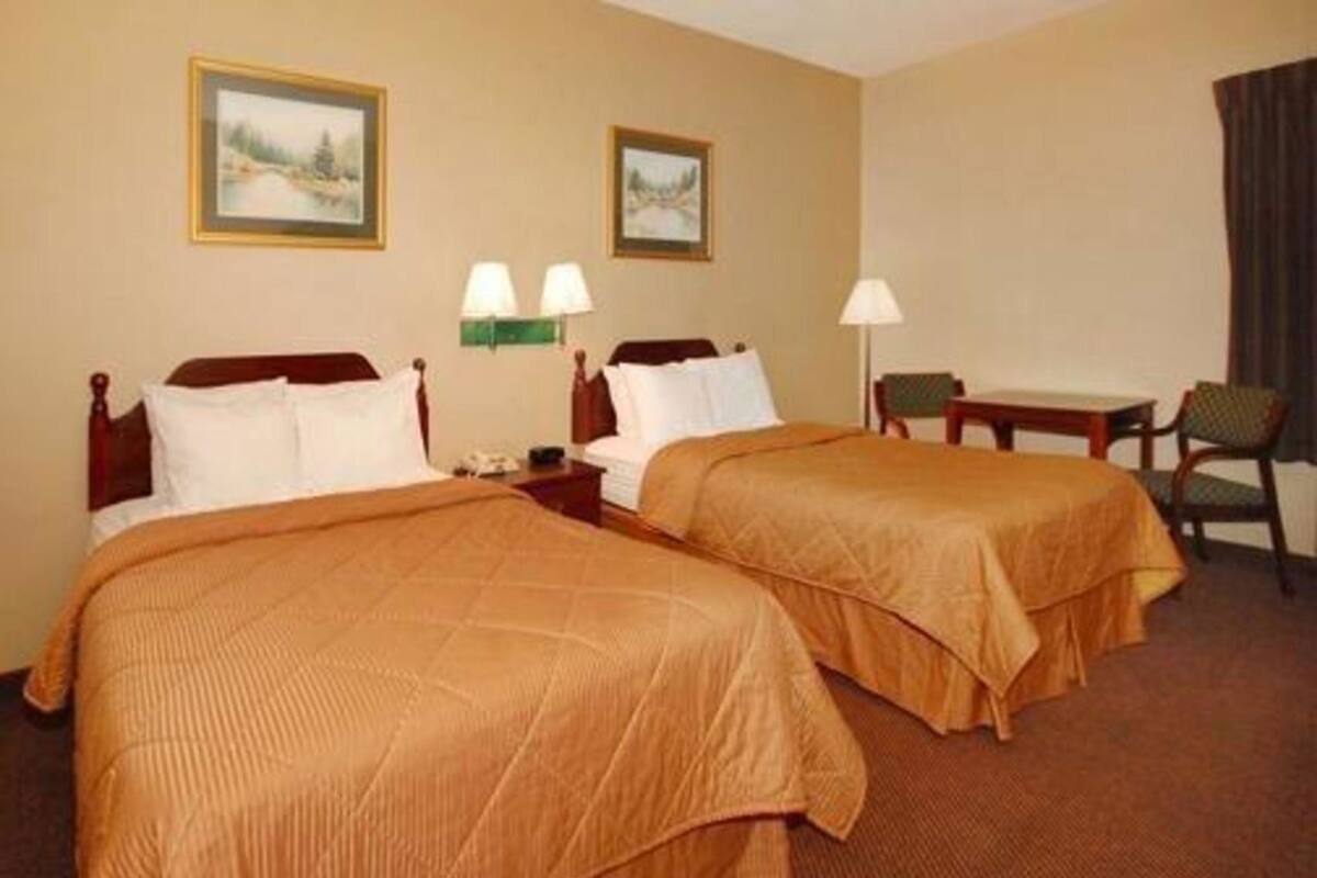 A hotel room with two beds, a desk, two lamps, and two framed pictures on the wall.