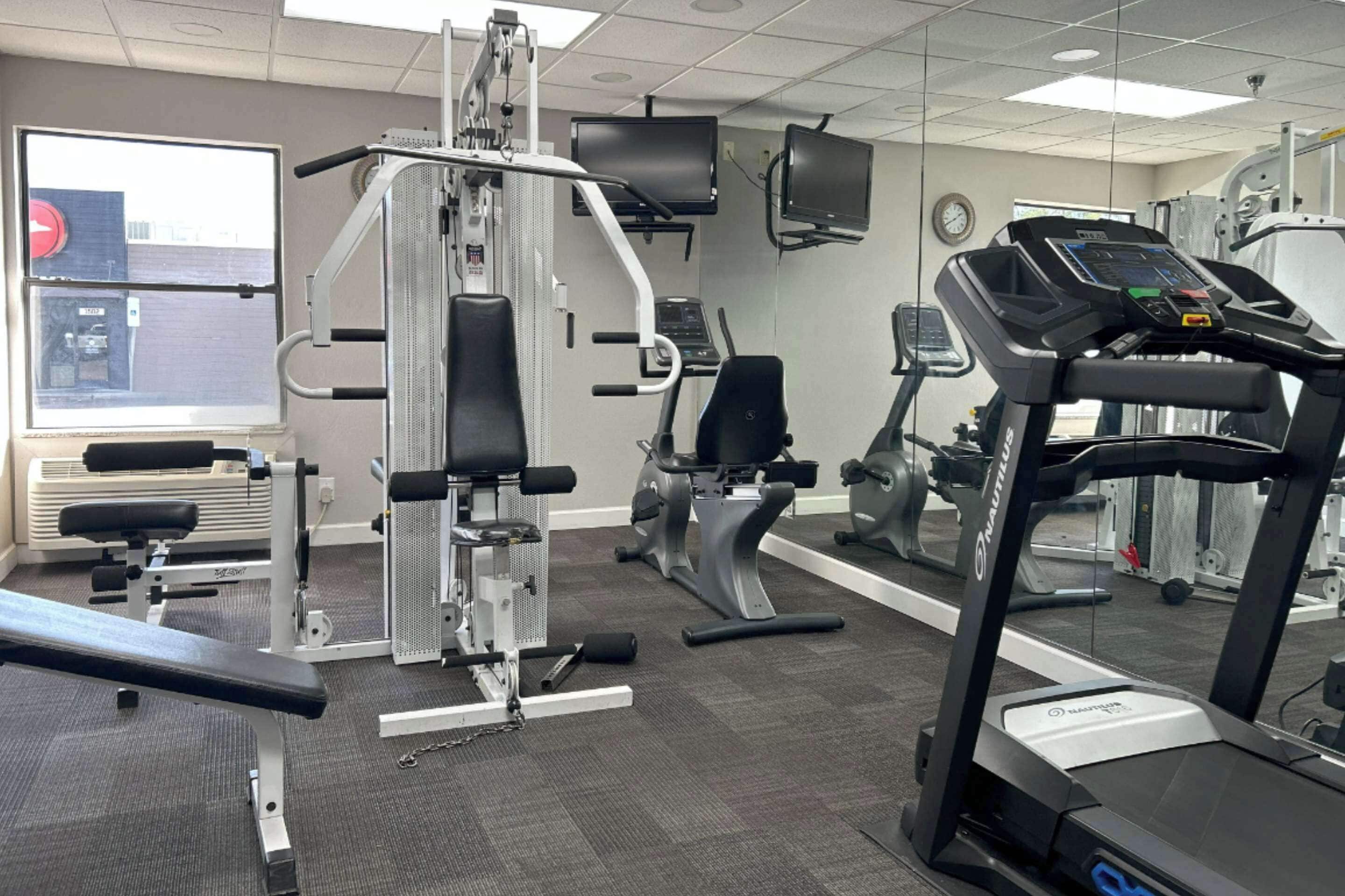 Un gimnasio con diversos equipos de ejercicio, incluyendo una cinta de correr, máquinas de pesas y un banco.