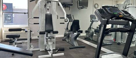 Un gimnasio con diversos equipos de ejercicio, incluyendo una cinta de correr, máquinas de pesas y un banco.