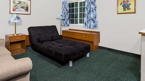 A room with a black sofa, a wooden nightstand, a small wooden dresser, and a window with blue curtains.