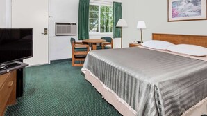 A hotel room with a bed, a TV, a desk with a chair, a window with curtains, and a painting on the wall.