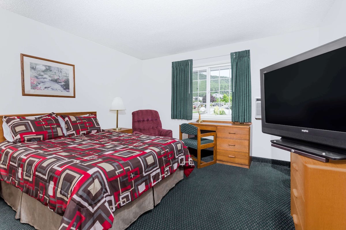 Habitación de hotel con cama, escritorio, silla, televisor y ventana con cortinas.