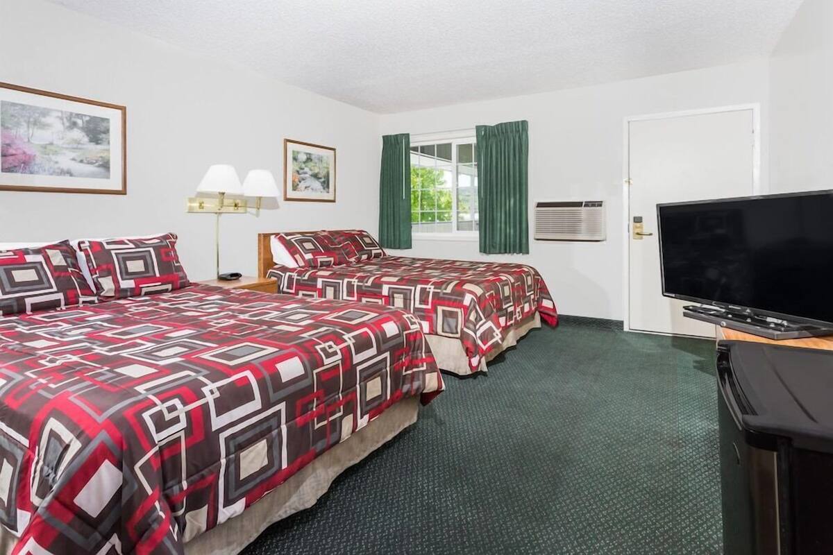 Habitación de hotel con dos camas, televisión, ventana con cortinas, lámpara y un cuadro en la pared.