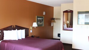 Quarto de hotel com uma cama grande, uma mesa de cabeceira, um abajur, um quadro, um espelho e vista para o exterior.