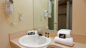 Casa de banho de hotel com lavatório, espelho, secador de cabelo e toalhas.