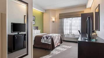 Una habitación de hotel con una cama, un escritorio con computadora, televisión y un refrigerador pequeño.