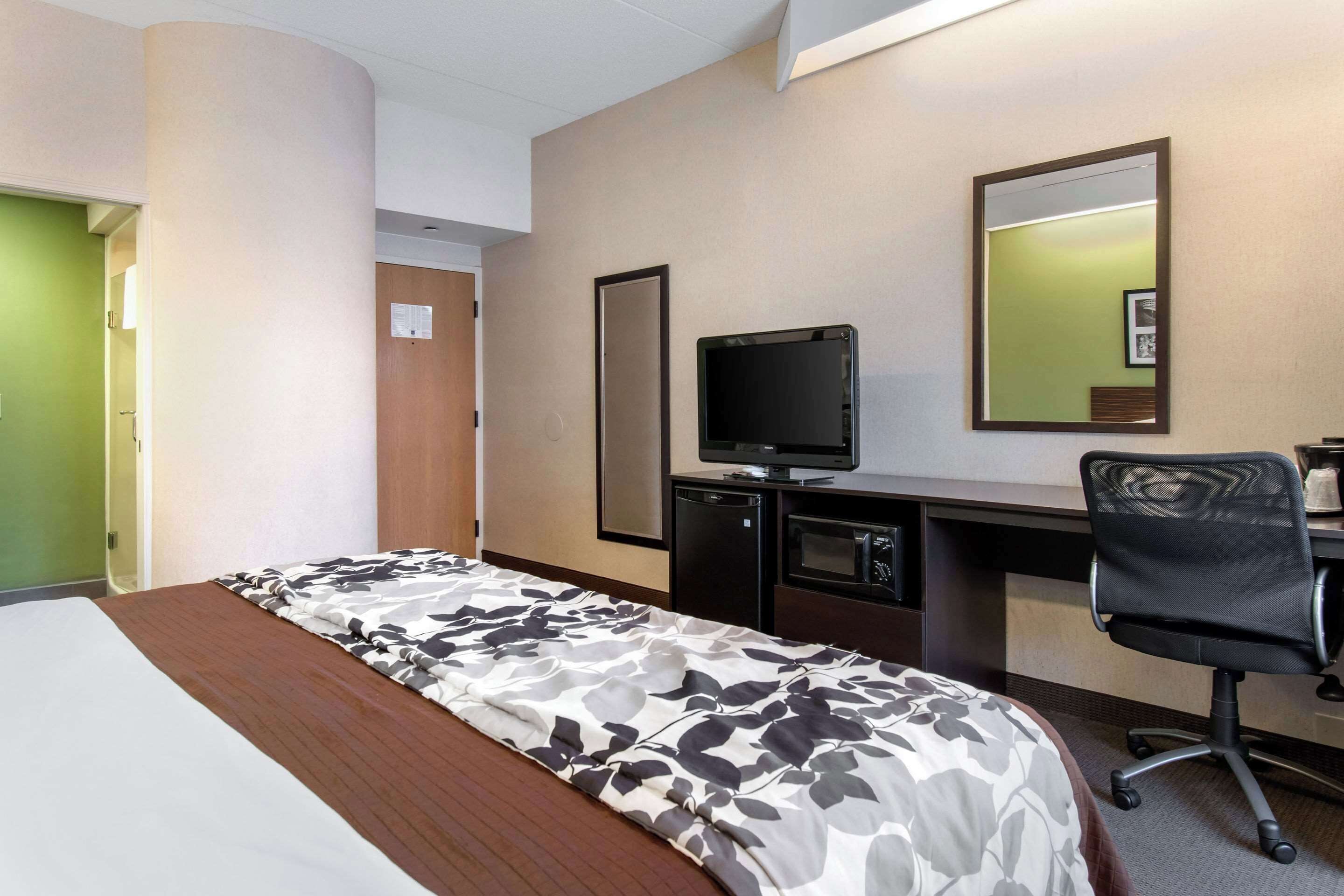 A hotel room with a bed, a desk with a computer, a chair, and a television.