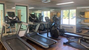 Un gimnasio con cintas de correr, bicicletas estáticas y un espejo grande.