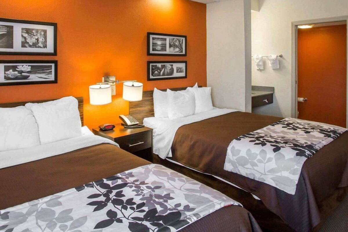 A hotel room with two beds, a nightstand with a lamp, and framed pictures on the wall.